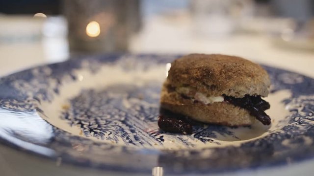Close up on hands, each pick up homemade scone with cherry jam and clotted cream. After that they bang together and say toast, cheers with pudding. Served on blue and white traditional British plate. 