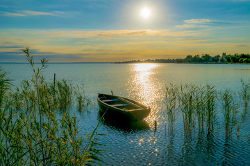 Rowing boat on lake at sunset.  Small wooden rowing boat on a calm lake at sunset. - obrazy, fototapety, plakaty
