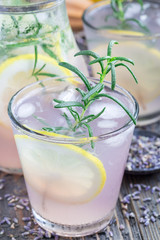 Homemade lemonade with lavender, fresh lemons and rosemary on wooden table, vertical, closeup