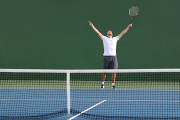 Tennis player man winning match happy excited with arms up in success on green outdoor court.