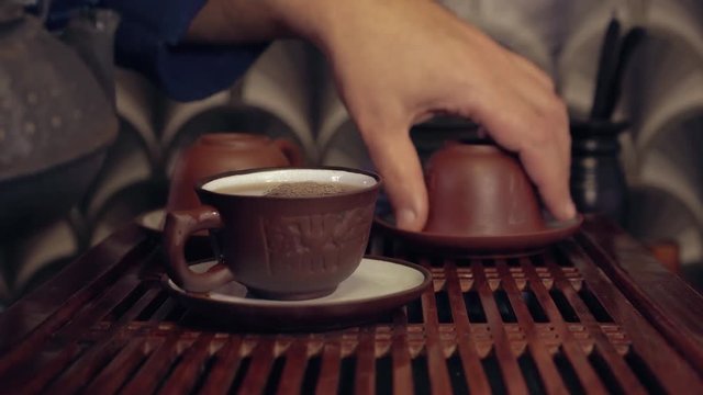 The action of traditional Chinese tea ceremony. Pouring tea from clay tea pot in a cup. Two tea pots in soft focus on the background.
