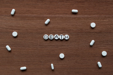 Pills with inscription "DEATH" on brown wooden surface background