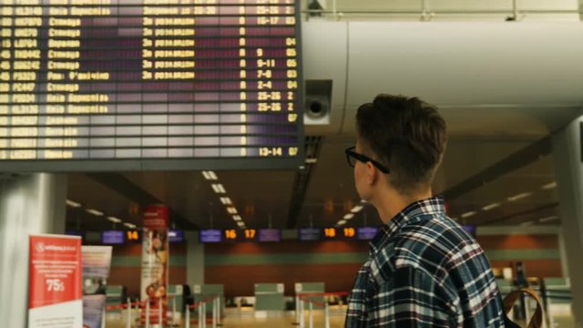 Portrait of young man with glasses checking his flight from the arrivals table in the airport.