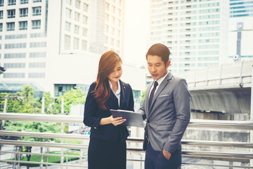 Business man pointing at document with smile and discussing something with her coworker while standing in front of office.