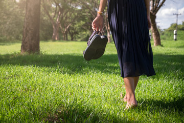 Slim girl walking barefoot on the grass holding her high heel shoes in hand