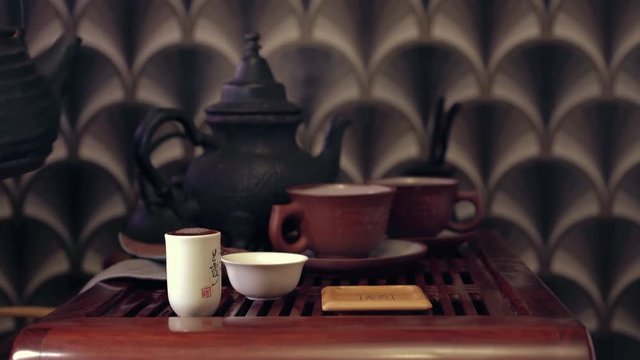 The action of traditional Chinese tea ceremony. Pouring tea from tea pot in a cup, putting it on bamboo coaster and serving it to a guest. Wooden tea board (chaban) on the background.