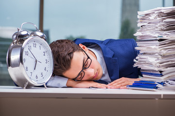 Businessman with pile stack of paper paperwork and an alarm cloc
