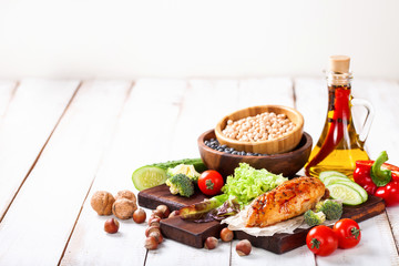 The baked chicken fillet and vegetables. Healthy and fitness food. Meat, salad, vegetables, nuts, beans on a light wooden background. Selective focus. Copy space