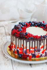 Bright festive cake with berries and chocolate on a white wooden background