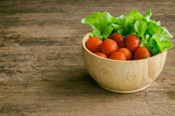 Fresh tomato and lettuce in wood bowl put on wood table. Side view of tomato and green oak lettuce with copy space for background. Fresh green oak lettuce and tomato prepare for cooking.