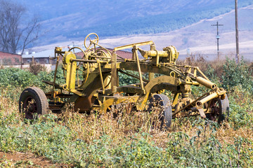 Fototapeta premium Vintage Yellow Farm Implement Against Rural Farm Landscape