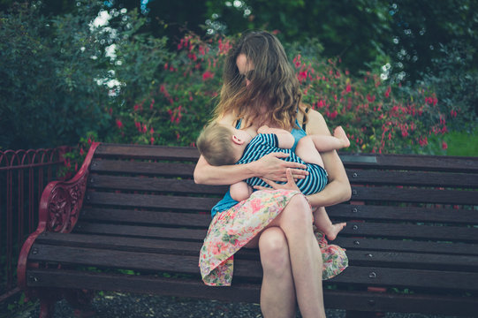 Mother breastfeeding baby on park bench