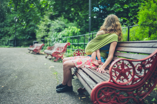 Mother with baby in sling resting on park bench