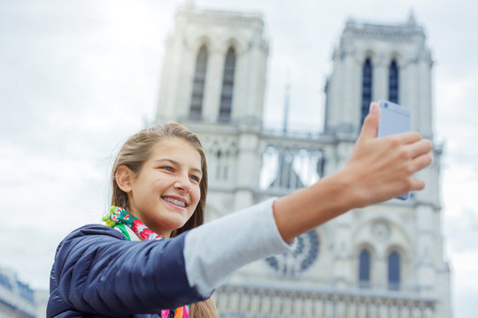 Teenager tourist girl is taking selfie with cathedral of Notre Dame de Paris. France.