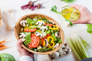 man pouring olive oil into healthy salad on kitchen