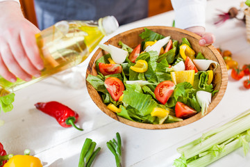 man pouring olive oil into healthy salad on kitchen