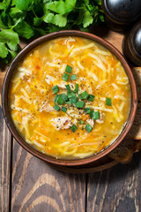 chicken soup with egg noodles in a bowl on wooden background, vertical top view