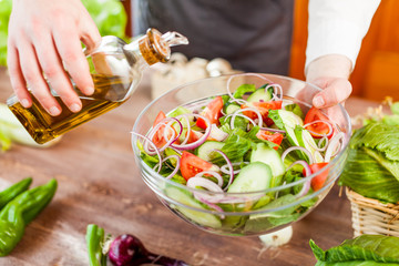 man pouring olive oil into healthy salad on kitchen