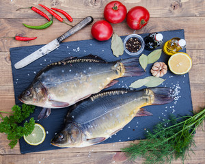 Fresh raw river mirror common carp fish on black stone cutting board on wooden table. Food ingredients for preparing. Cooking and kitchen concept background. Healthy seafood. Lemon, herbs and spices.