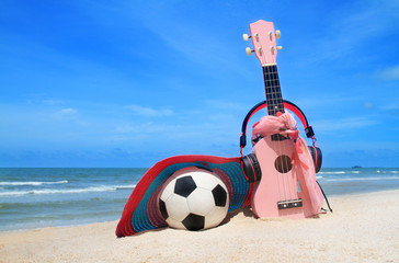 pink headphones ukulele and handcraft hat football on blue sky and beach background