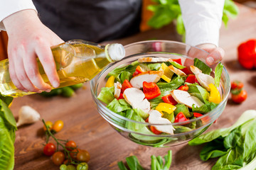 man pouring olive oil into healthy chicken salad on kitchen