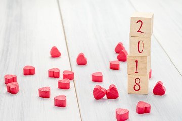 New year 2018 number on wood stack cube with group of mini red heart on white wood plank table,Holiday celebrate greeting card