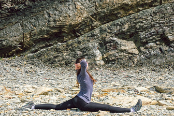 Side view of a healthy mature woman figure stretching and exercising on a rock platform