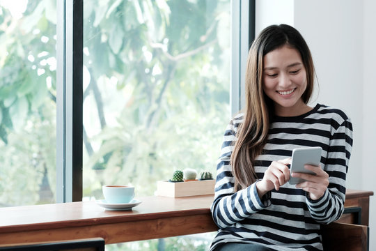 Young asian woman using smart phone while sitting bay window cafe background, People technology and lifestyle