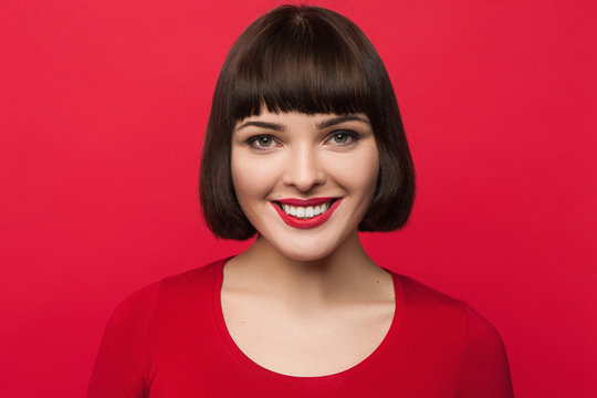 Joyful young woman openly smiling on pop red backdrop. Happiness background. Good news for pretty girl, lively face, fortune concept