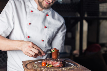 Chef in hotel or restaurant kitchen cooking, only hands. He is working on the micro herb decoration
