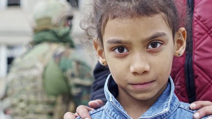 PAN of shy little Arab girl with curly hair looking into camera; unrecognizable man standing behind her