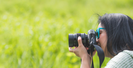Woman photographer wear sunglasses and holding camera and take a picture of green grass field,Travel wanderlust concept,Banner size leave space for adding text or content for advertise on website