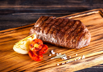Medium rare grilled Steak Ribeye with fried onions and cherry tomatoes on a wooden board