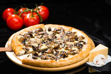 selective focus on sliced piece of appetizing Italian cheese pizza with marinated mushrooms on the foreground, and whole pizza on the background