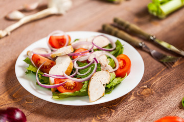 Fresh salad with chicken, tomato and greens on wooden background top view. Healthy food.