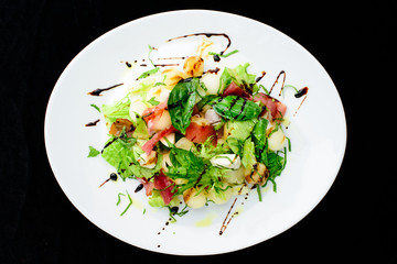 classic Italian summer delicious fresh salad with cheese, parma ham and soy sauce on white plate, on dark background, top view