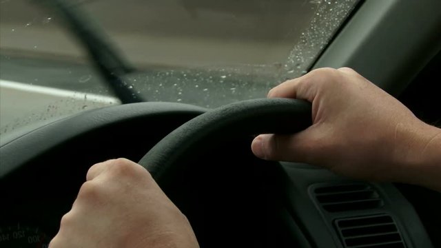 Driving on highway, rain. Detail of two Hands on the steering wheel, windshield POV. Right side wheel / driving - UK 
