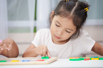 Cute little child girl having fun to play and learn magnetic alphabets on board in the room