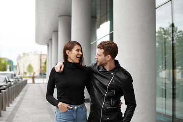 Outdoor lifestyle portrait of cheerful and cute young Euroepan couple or family spending nice time outside at weekend, hugging, talking, walking on streets of big city, enjoying each other's company