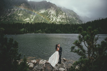 Young happy couple standing on the shore of the lake and admire the mountain scenery in Romania