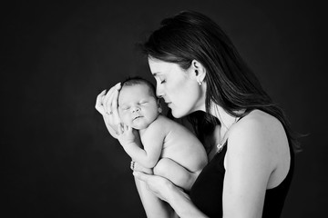 Mother kissing and hugging newborn son at gray background, tender, care, love © Tomsickova