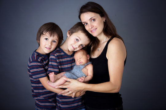 Family picture of three boys and their mom, kissing and hugging newborn baby