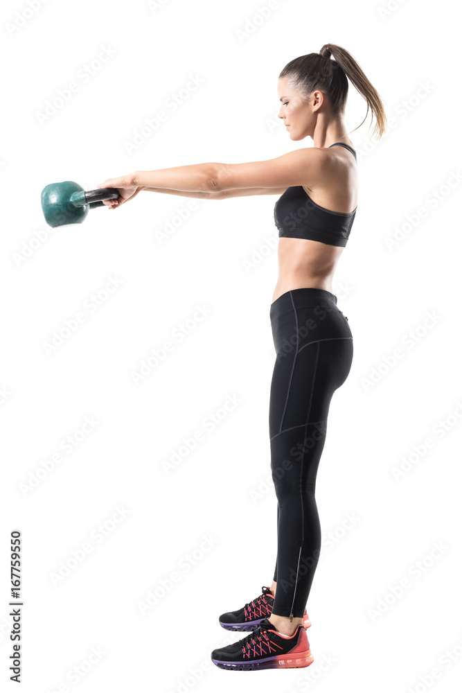 Wall mural Side view of strong sporty fitness woman swinging 12 kg kettlebell in mid air motion. Full body length portrait isolated on white studio background