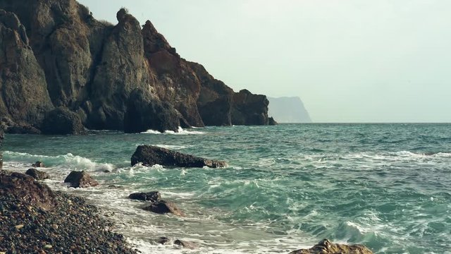 Waves washing the pebble beach. Waves lapping agains a shingle beach. Sea scenery with old mountains on background.