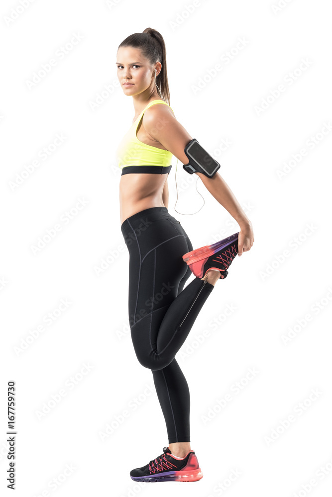 Wall mural side view of female athlete stretching leg quadriceps muscles while warming up. full body length por - Wall murals