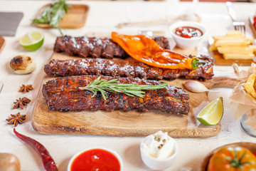 Spicy hot grilled spare ribs from a summer BBQ served with chips, corn and fresh tomatoes on an old wooden cutting board