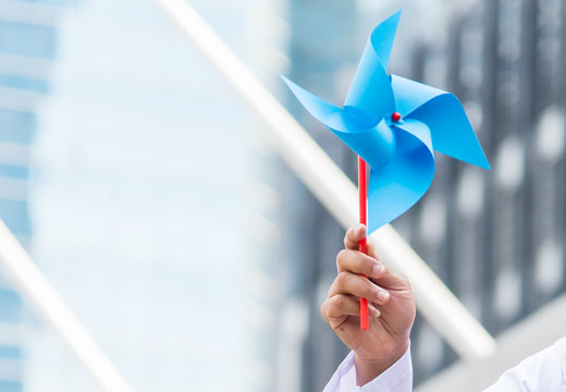 Portrait of hand with wind turbine paper, save energy concept, city background.