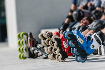 Fototapeta na wymiar Feet of rollerbladers wearing inline roller skates sitting in outdoor skate park, Close up view of wheels befor skating