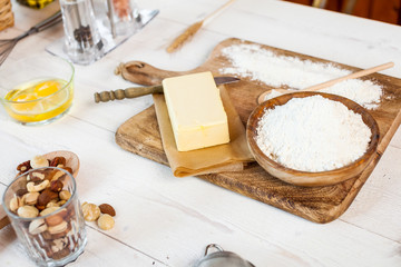 Fototapeta premium Baking ingredients in rural kitchen - dough recipe ingredients (eggs, flour, milk, butter, sugar) and rolling pin on wooden white table.