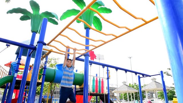 Slow motion of happy Young asian boy hang the yellow bar by his hand to exercise at out door playground under the strong sunlight in summer time.
